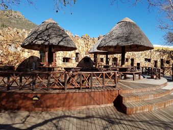 Ntshondwe Camp swimming pool and thatched buildings beneath the mountain cliffs